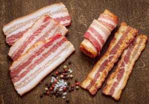 Lanières de bacon de bœuf cru et cuit sur une surface en bois rustique — Boucherie Beirut