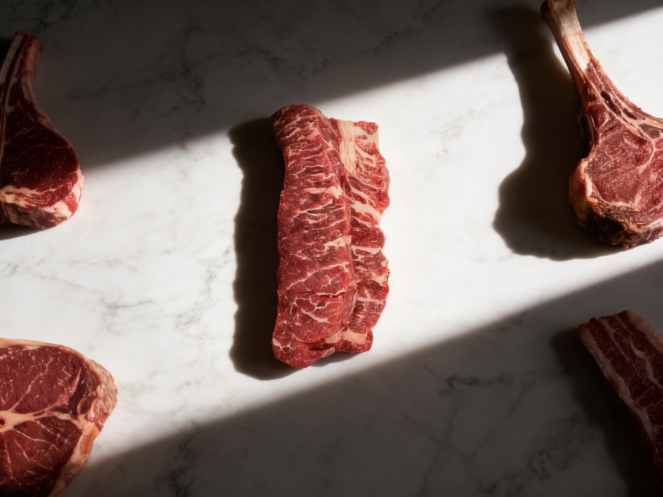 Raw Denver steak in the spotlight surrounded by ribeye and tomahawk cuts on marble – Boucherie Beirut Laval