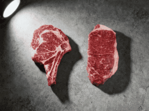 Ribeye vs strip steaks side by side on concrete surface showing marbling difference — Boucherie Beirut