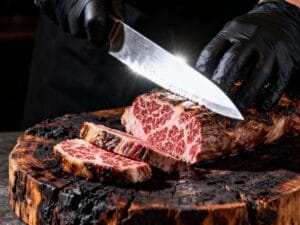 Black-gloved hands slicing a grilled Wagyu steak on a charred wood board revealing perfect medium-rare marbling – Boucherie Beirut Laval