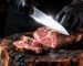 Black-gloved hands slicing a grilled Wagyu steak on a charred wood board revealing perfect medium-rare marbling – Boucherie Beirut Laval