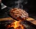 Halal burger patty lifted on a spatula over charcoal flames on a BBQ grill – Boucherie Beirut Laval