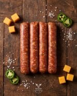 cheddar-jalapeno-beef-sausage-boucherie-beirutjpg | Boucherie Beirut Cheddar jalapeño beef sausage with cheddar cubes and jalapeño slices on a rustic wooden surface – Boucherie Beirut Laval