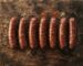 Seven halal beef sausages arranged in a row with spices on a rustic wooden surface – Boucherie Beirut Laval