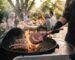 Halal BBQ pitmaster grilling tomahawk steak and beef sausages on charcoal with family gathering in background – Boucherie Beirut Laval