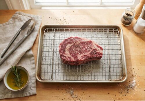 Thick ribeye steak seasoned with salt and pepper on a wire rack ready for reverse sear in the oven