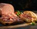 Halal mortadella sliced fresh on a walnut board next to a ciabatta sandwich with melted provolone